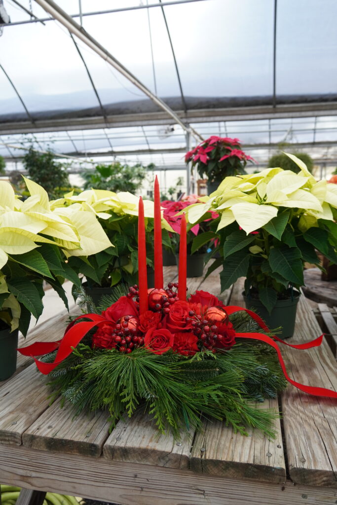 red flower arrangement perched on a wreath of fresh greenery with three red candles