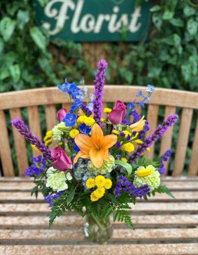Floral arrangement in vase with colorful, purple, blue, orange, and yellow flowers.