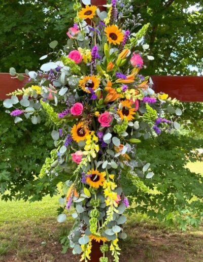 Cross floral tribute with sunflowers, sage, roses, and flowers.