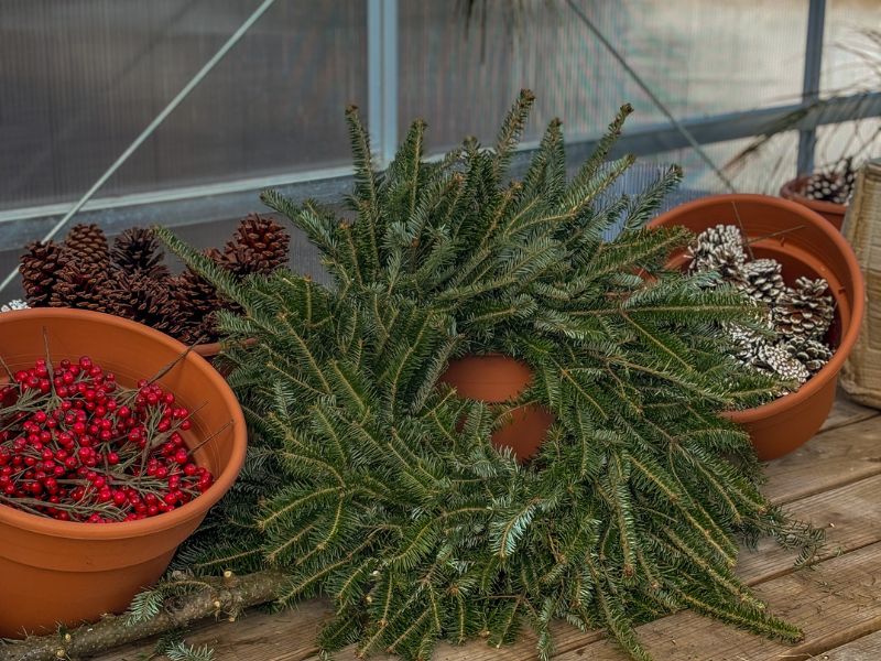 wreath-making-station (1) wreath on a workbench surrounded by pine cones and holly berries